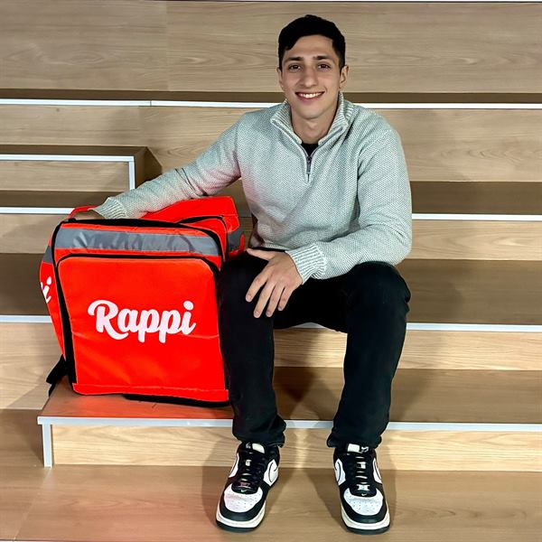 Ramiro Farjat sonriendo, sentado junto a una mochila de reparto de Rappi